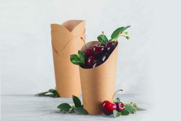 Craft paper eco-friendly food packaging with cherries. Disposable cups on a neutral gray background with copy space. Preserving nature and recycling concept.